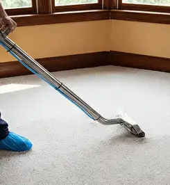 Steam carpet cleaning technician using a hot-water extraction wand on a residential carpet, wearing blue protective shoe covers Allentown, PA.